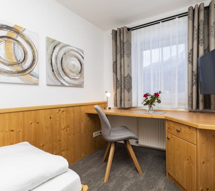 Bett, Tisch mit Stuhl und TV im Einbettzimmer